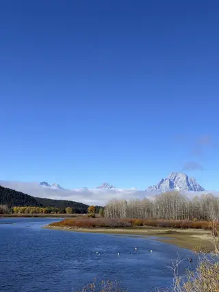 蓝色湖面、秋色树林和云上的雪山